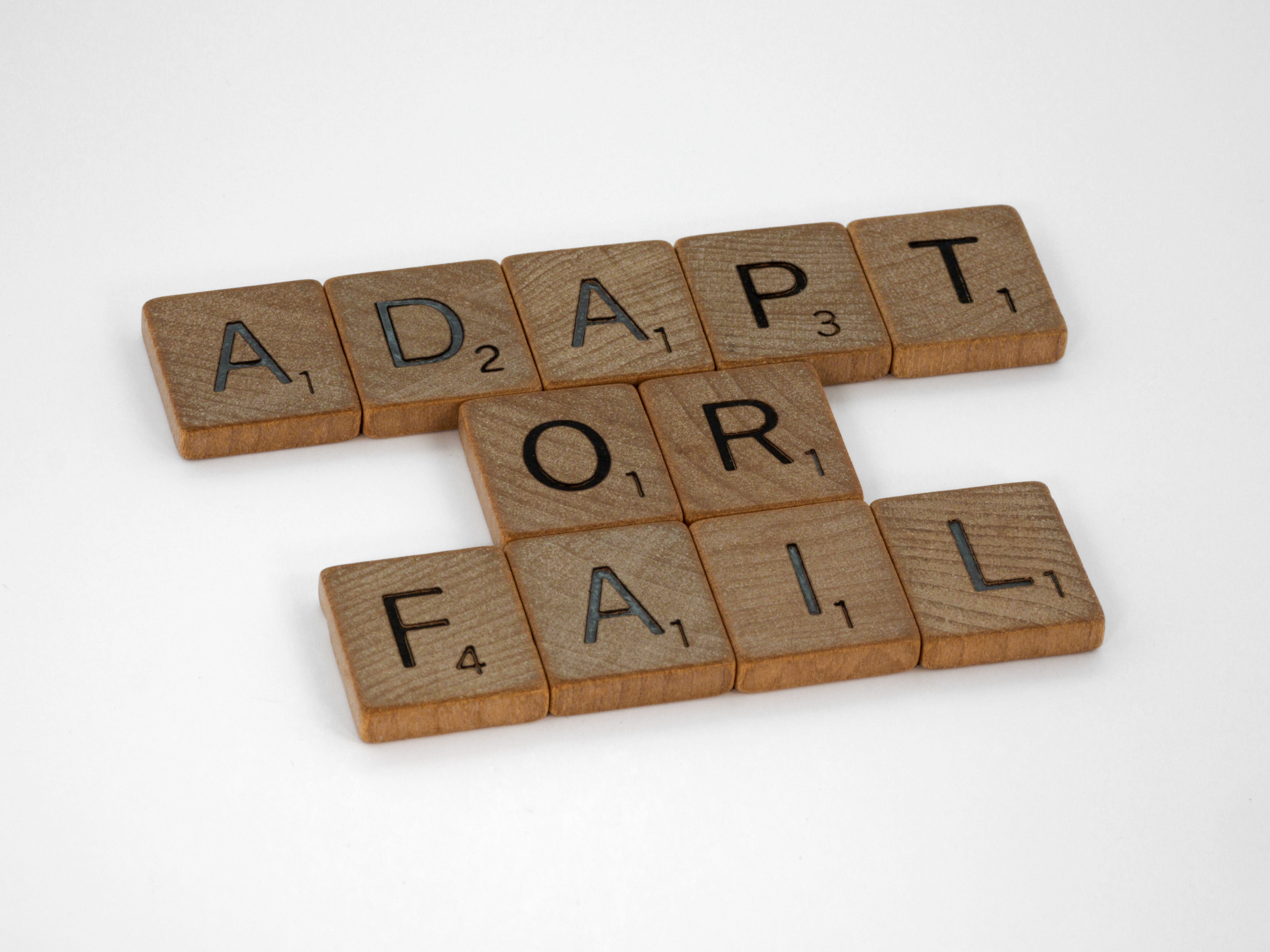 Scrabble tiles spelling out ADAPT OR FAIL on a white surface